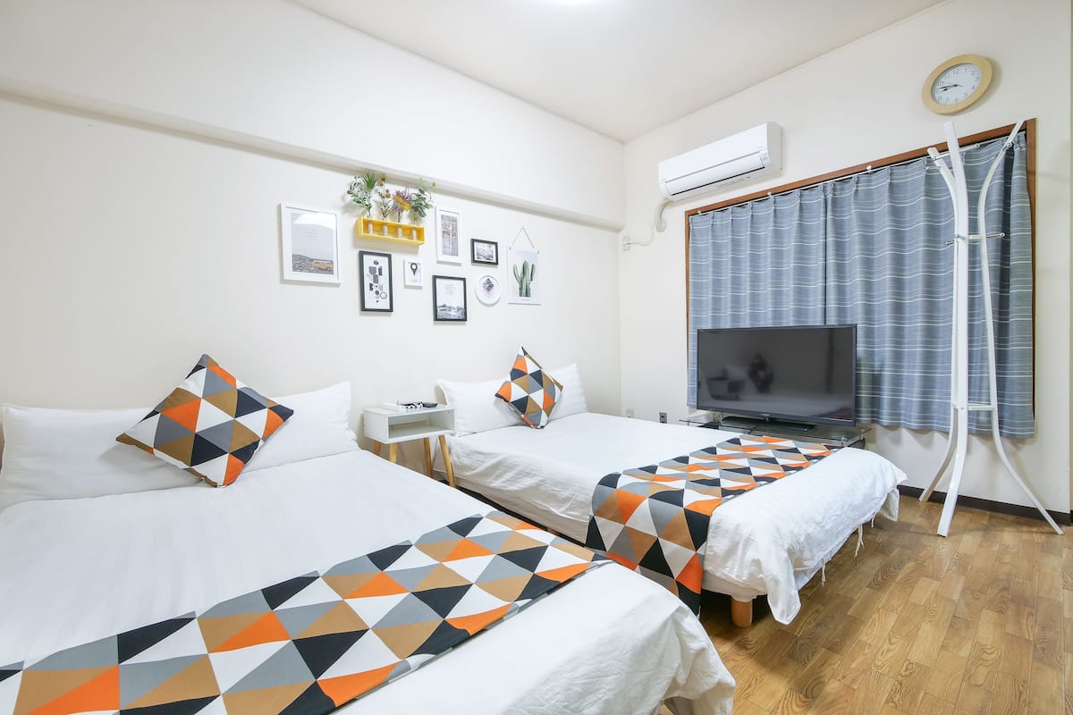 A hotel room with two beds, a TV, a desk, and a window with curtains.