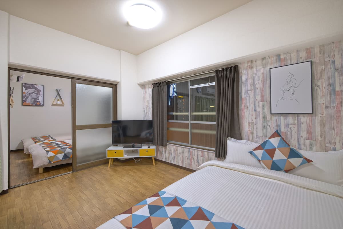 A hotel room with a bed, a TV, a desk, and a window with curtains.
