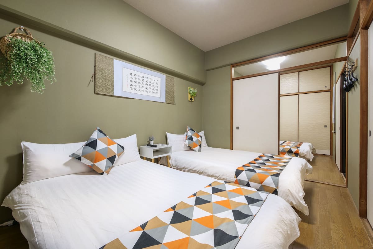A hotel room with two beds, a small desk, a wall-mounted plant, and a sliding door closet.