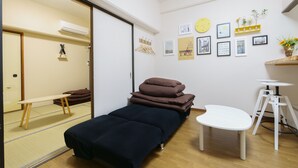 Una habitación con una cama, una mesita y una estantería con objetos decorativos.