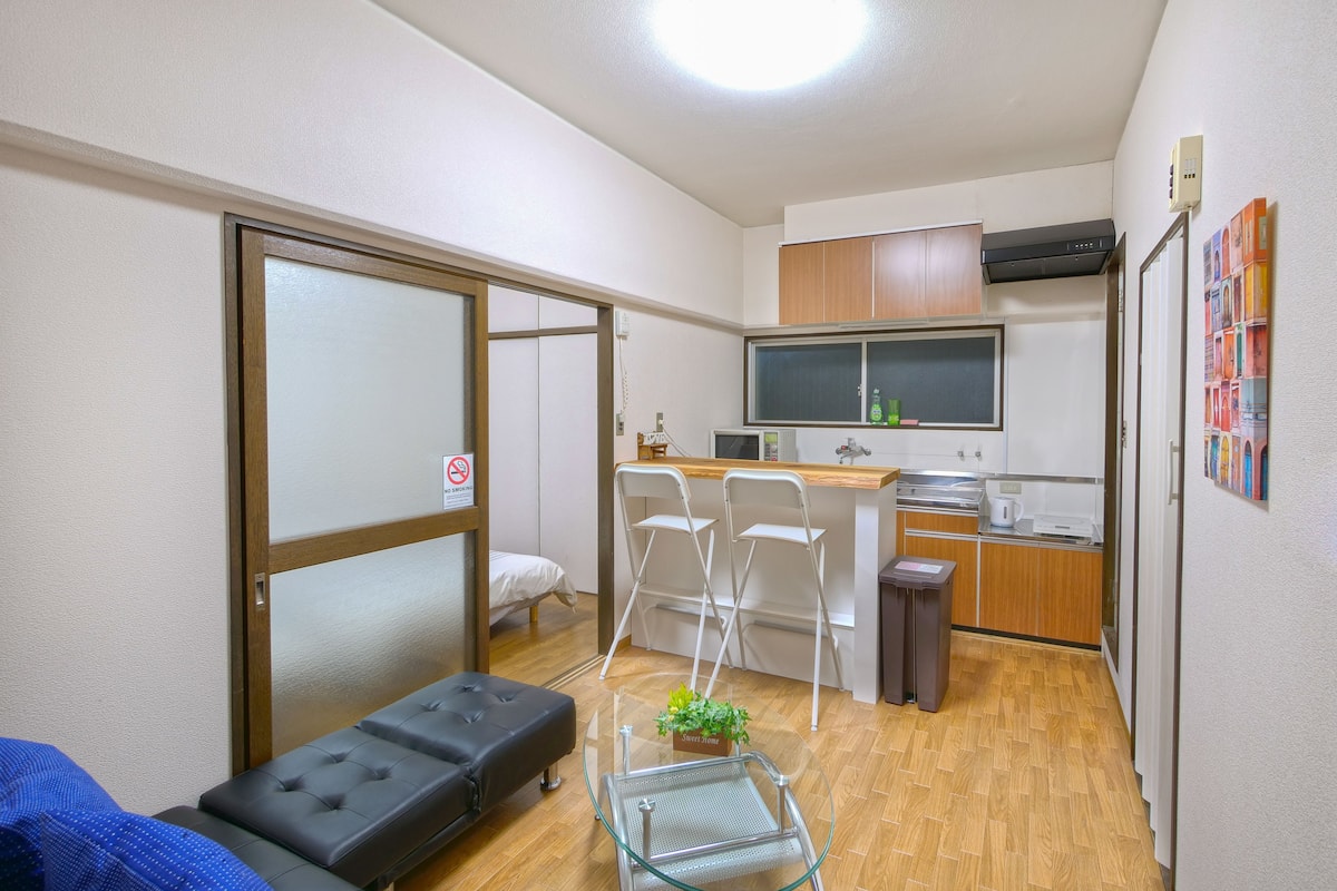 A compact room with a bed, a small kitchenette, and a dining area with chairs.
