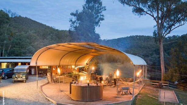 A large, semi-transparent tent with a central fire pit, surrounded by a gravel area and a wooden deck. - Fawlty Farm in Taylor Bay with 3 FREE experiences (Taylor Bay)