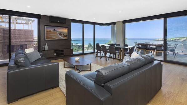 A modern living room with a large TV, a fireplace, and a view of the ocean. - Manhattan@SoHo - Ocean Views (Gerringong)