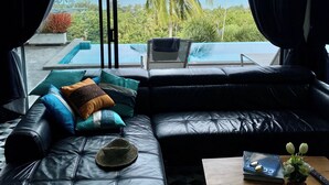 Un soggiorno moderno con un divano in pelle, un laptop e vista sull'oceano e palme.