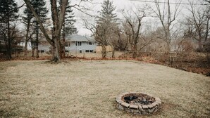 A backyard with a fire pit, a house, and leaf-covered ground. - Golf Course Views! Ranch! Fire Pit ! Bring Pets! (West Lafayette)