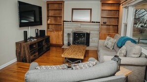 A living room with a fireplace, a television, wooden shelving, and a sofa. - Golf Course Views! Ranch! Fire Pit ! Bring Pets! (West Lafayette)