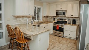 A kitchen with white cabinets, a granite countertop, a stainless steel stove, and a microwave. There are two wooden chairs at the island. - Golf Course Views! Ranch! Fire Pit ! Bring Pets! (West Lafayette)