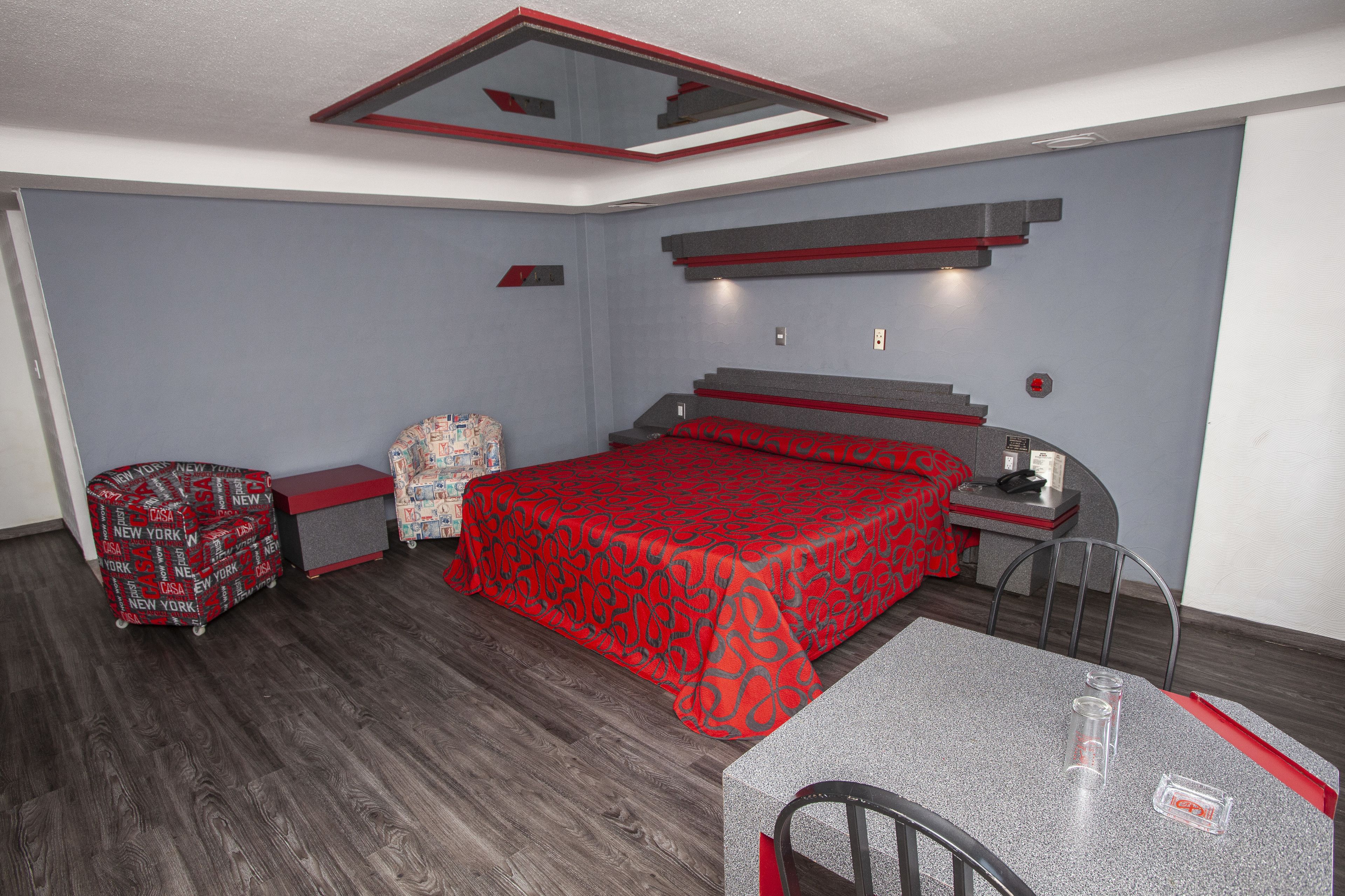 A modern bedroom with a red patterned bedspread, a desk with a chair, and a small table.