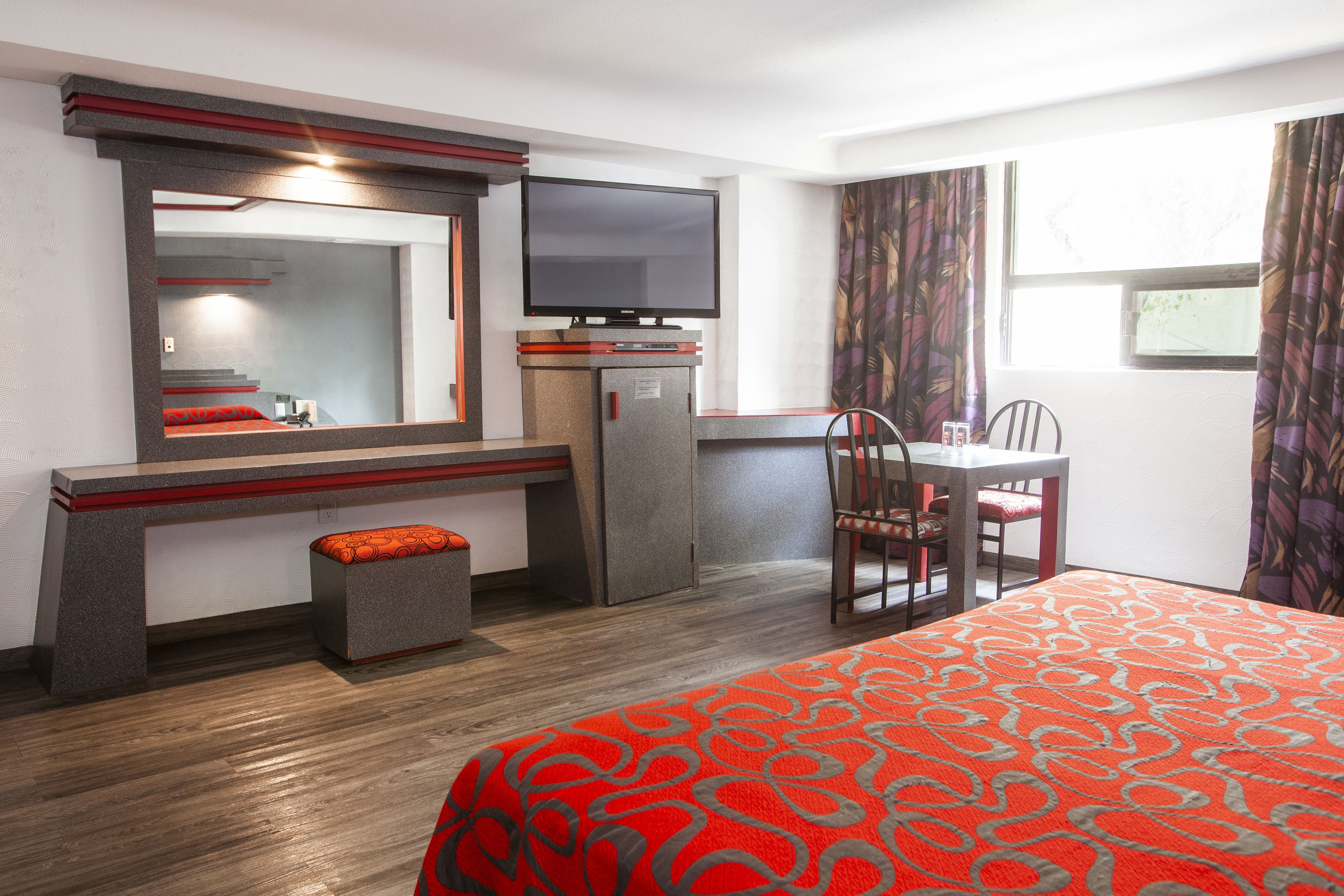 A hotel room with a bed, a desk with a chair, a television, and a small refrigerator.