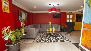 A modern lobby with a grey sofa, red walls, and a black and white patterned rug.