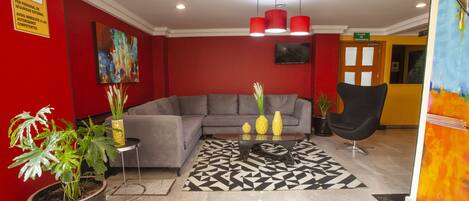 Un lobby moderno con un sofá gris, paredes rojas y un tapete blanco y negro.