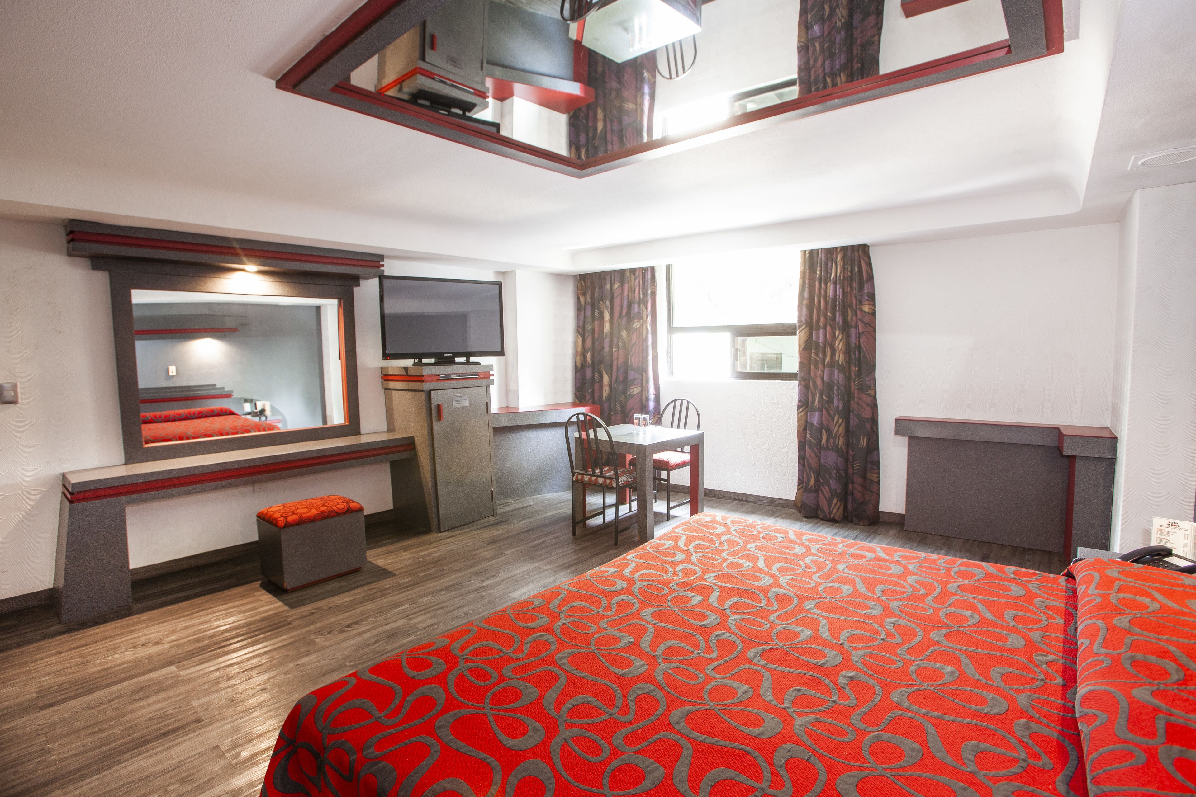 Una habitación de hotel con cama, escritorio con silla, televisor y ventana con cortinas.