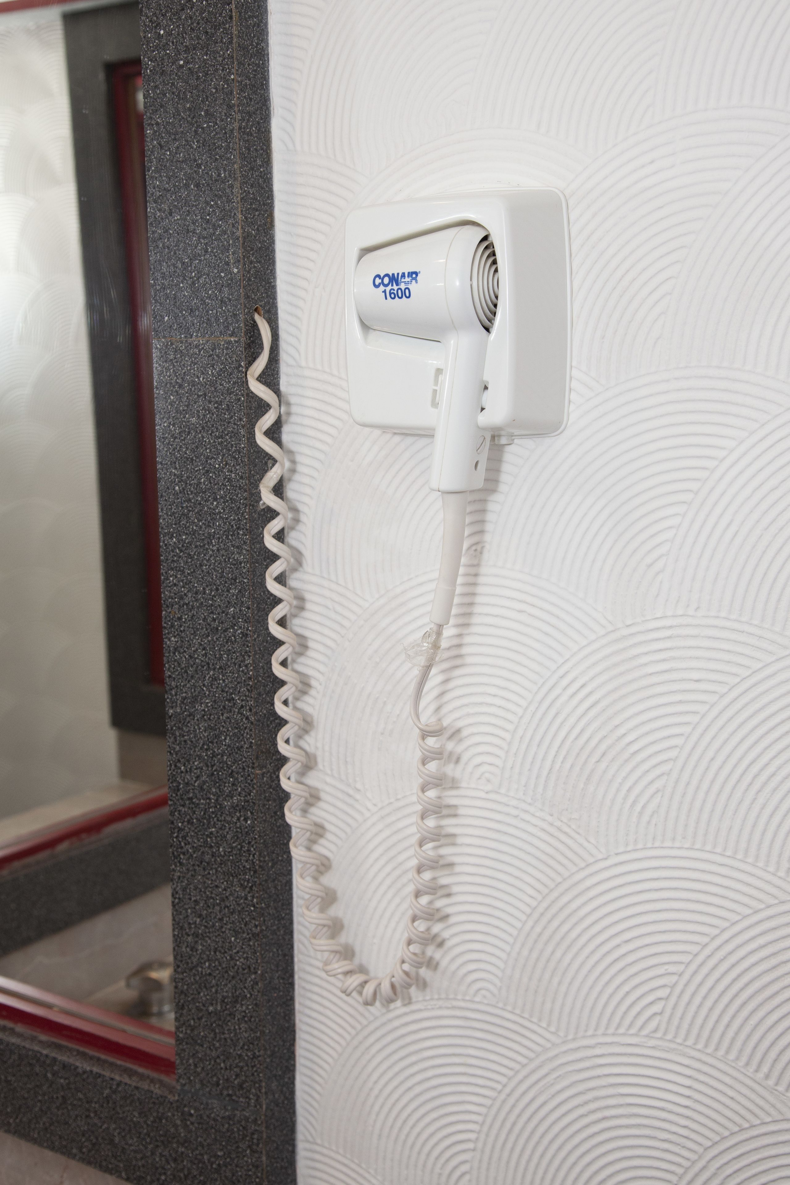 Een haardroger bevestigd aan een gestructureerde muur met een opgerolde kabel.