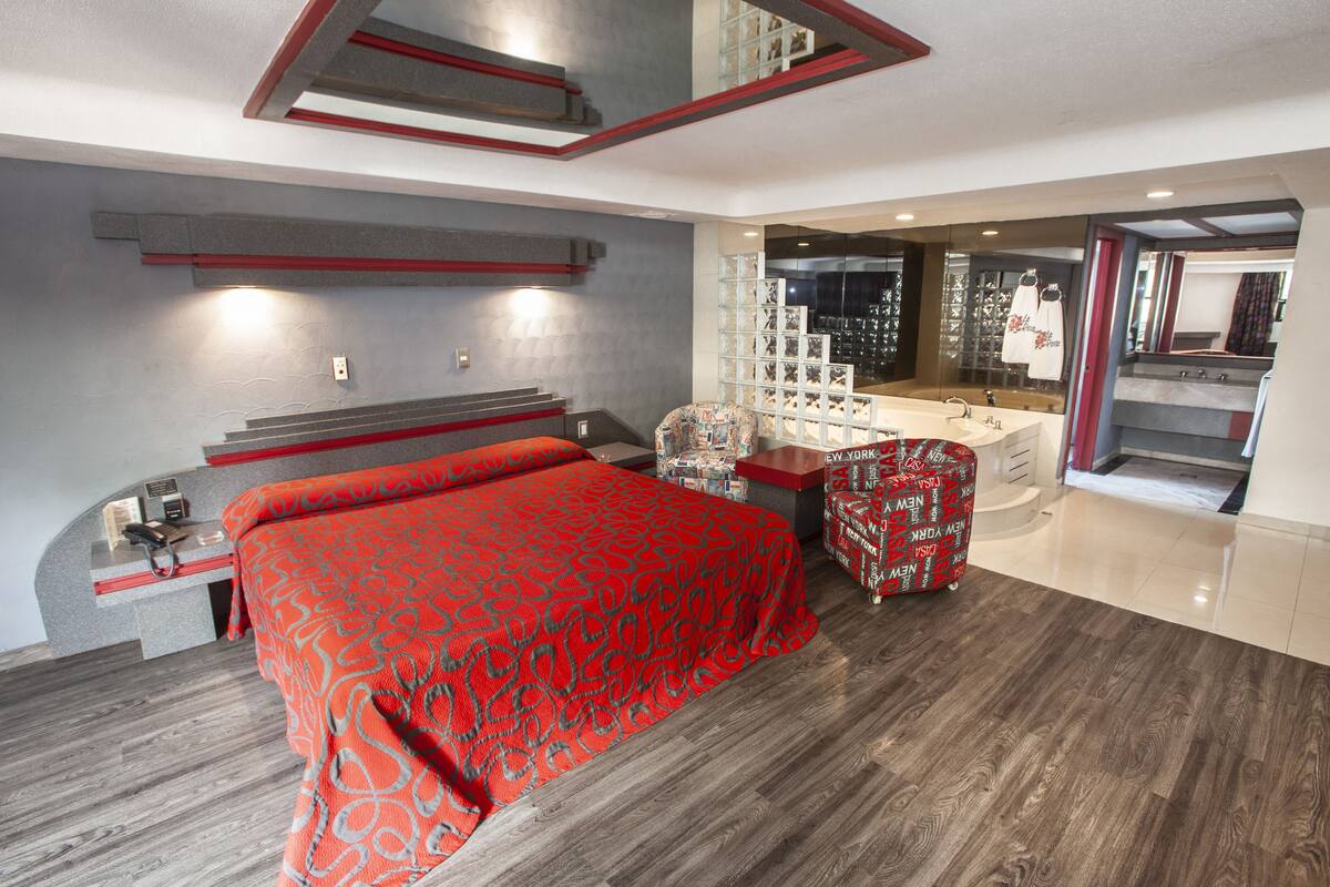 A modern hotel room with a large bed, a desk, and a vanity with a mirror.