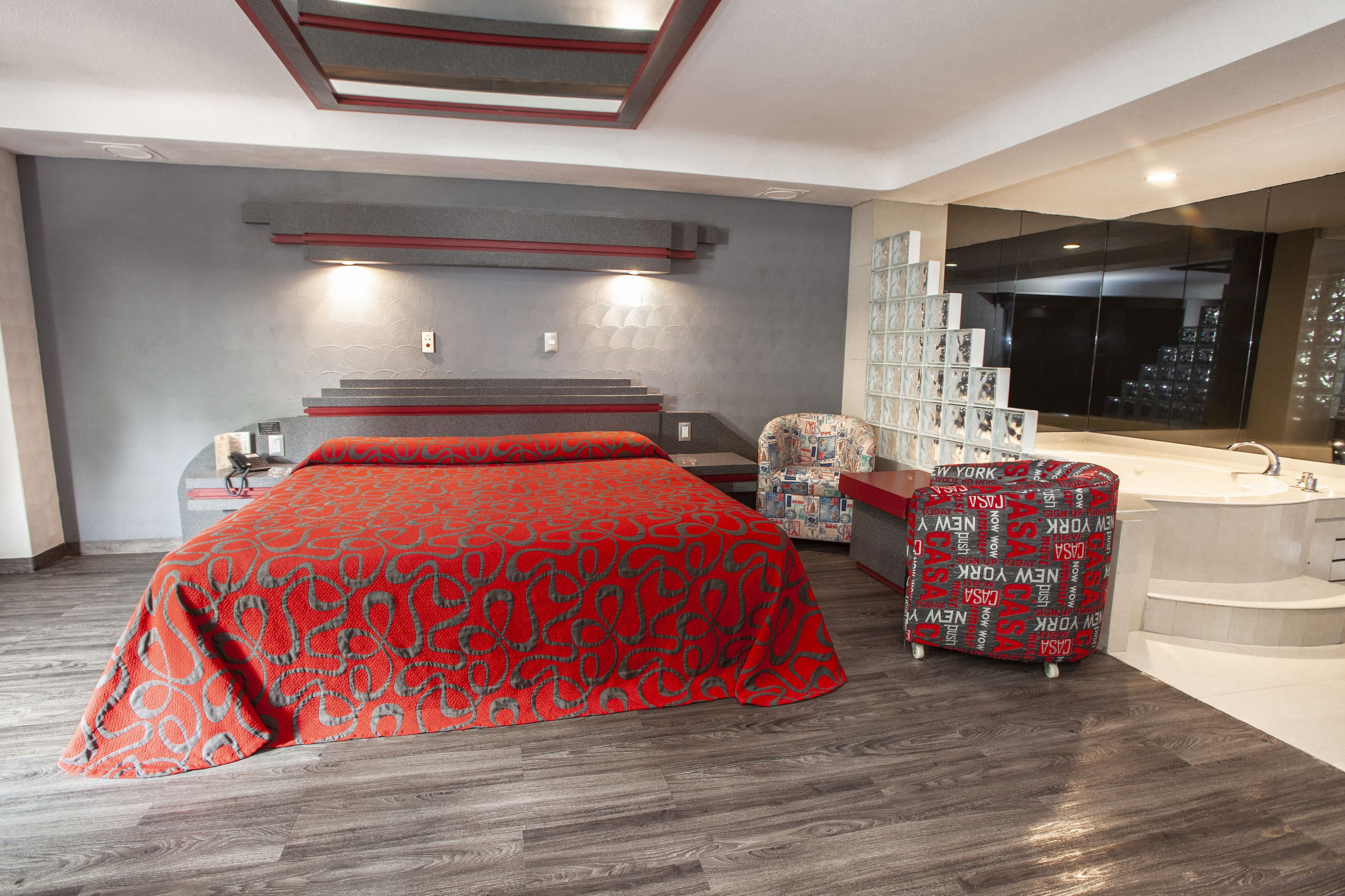 Une chambre moderne avec un grand lit, une coiffeuse avec un miroir et un coin salon agrémenté d’un pouf à motifs.