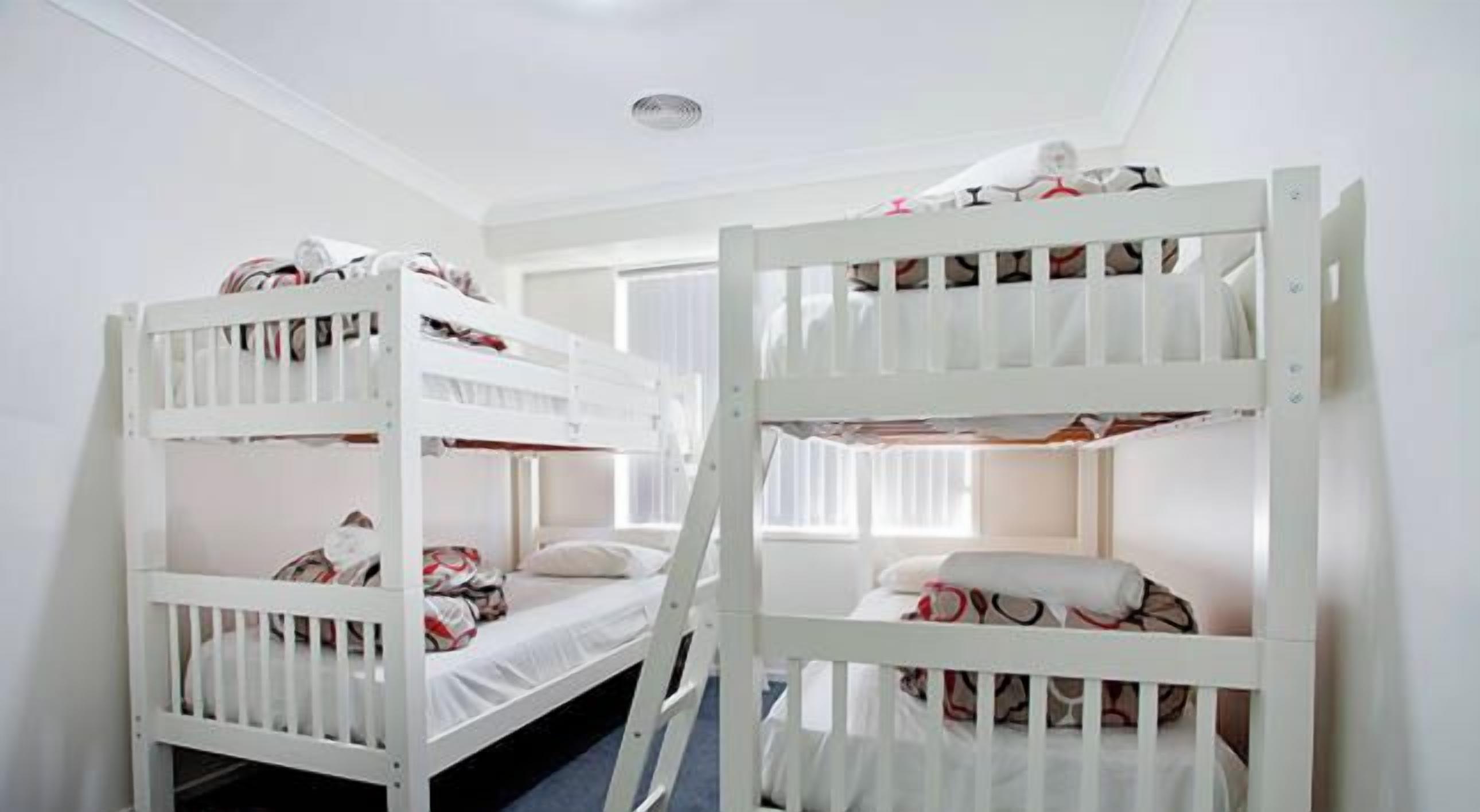 A room with bunk beds, a ladder, and a window with curtains.