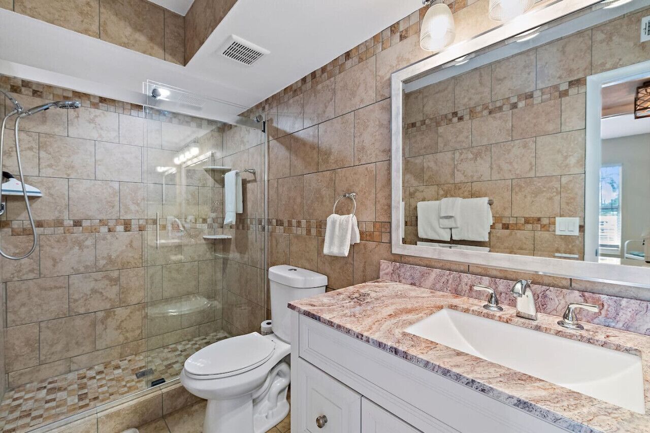 A modern bathroom with a glass-enclosed shower, a white toilet, a marble sink, and a large mirror.