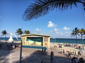 Een theater aan het strand met een podium, zitplaatsen, palmbomen en de oceaan op de achtergrond.