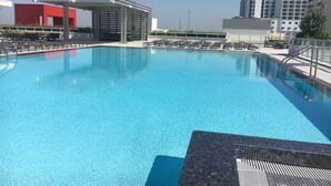 Une piscine dotée de chaises longues et d’un espace de repos couvert, le tout entouré de bâtiments modernes.
