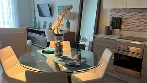 Une cuisine moderne avec un coin repas, comprenant une table ronde en verre, des chaises blanches et un four encastré.