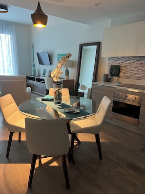 Een moderne keuken met een eethoek, met een ronde glazen tafel, witte stoelen en een inbouwoven.