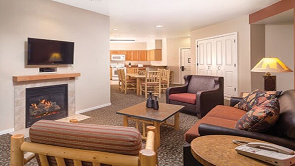 A living room with a fireplace, a television, a sofa, a coffee table, and a dining area in the background.