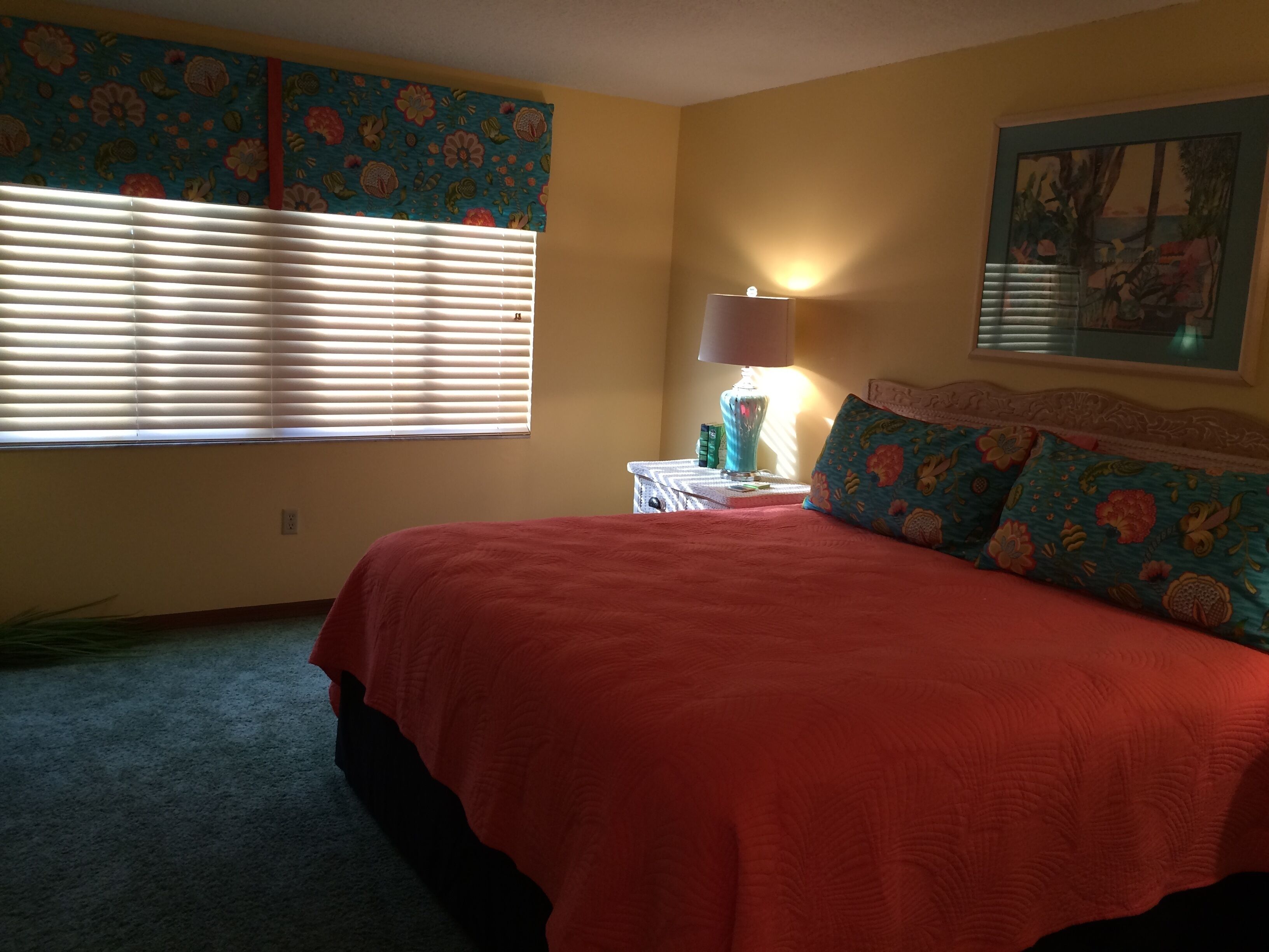 Une chambre à coucher comprenant un lit, une table de chevet, une lampe, une fenêtre avec des stores et une décoration murale à motifs floraux.