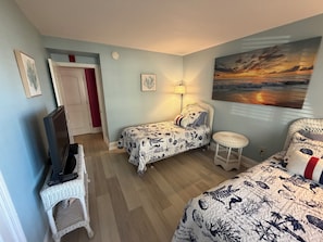 A room with a bed, a chair, a desk, a lamp, and a painting.