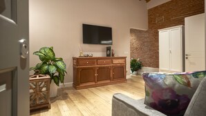 A living room with a wooden cabinet, a flat-screen TV, a brick wall, and a door. - "MATTONE" - Elegant apartment for 4 people on the 3rd floor. (Firenze)
