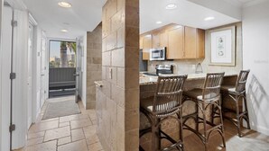 A kitchen with wooden cabinets, a microwave, and a bar area with wicker chairs. - Beautifully Updated & Decorated Gulf Side Garden View Condo (Siesta Key)