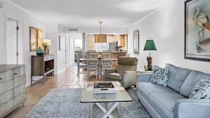A spacious living area with a sofa, coffee table, and dining table. A kitchen is visible in the background. - Beautifully Updated & Decorated Gulf Side Garden View Condo (Siesta Key)