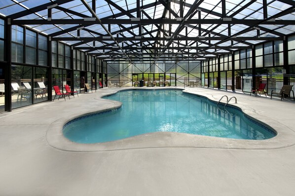 An indoor swimming pool with a glass ceiling, surrounded by lounge chairs and a concrete deck.