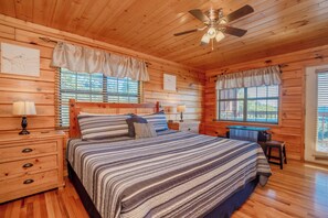 Une chambre dans une cabane en bois, avec un lit, des tables de chevet, un bureau et un ventilateur de plafond.