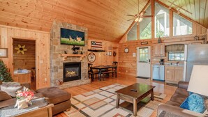 A wooden cabin interior with a fireplace, dining area, kitchen, and a large window. - 🏔️Private Sunsets🌅 Sunset Views, Hot Tub & Indoor Pool, near Dollywood (Sevierville)