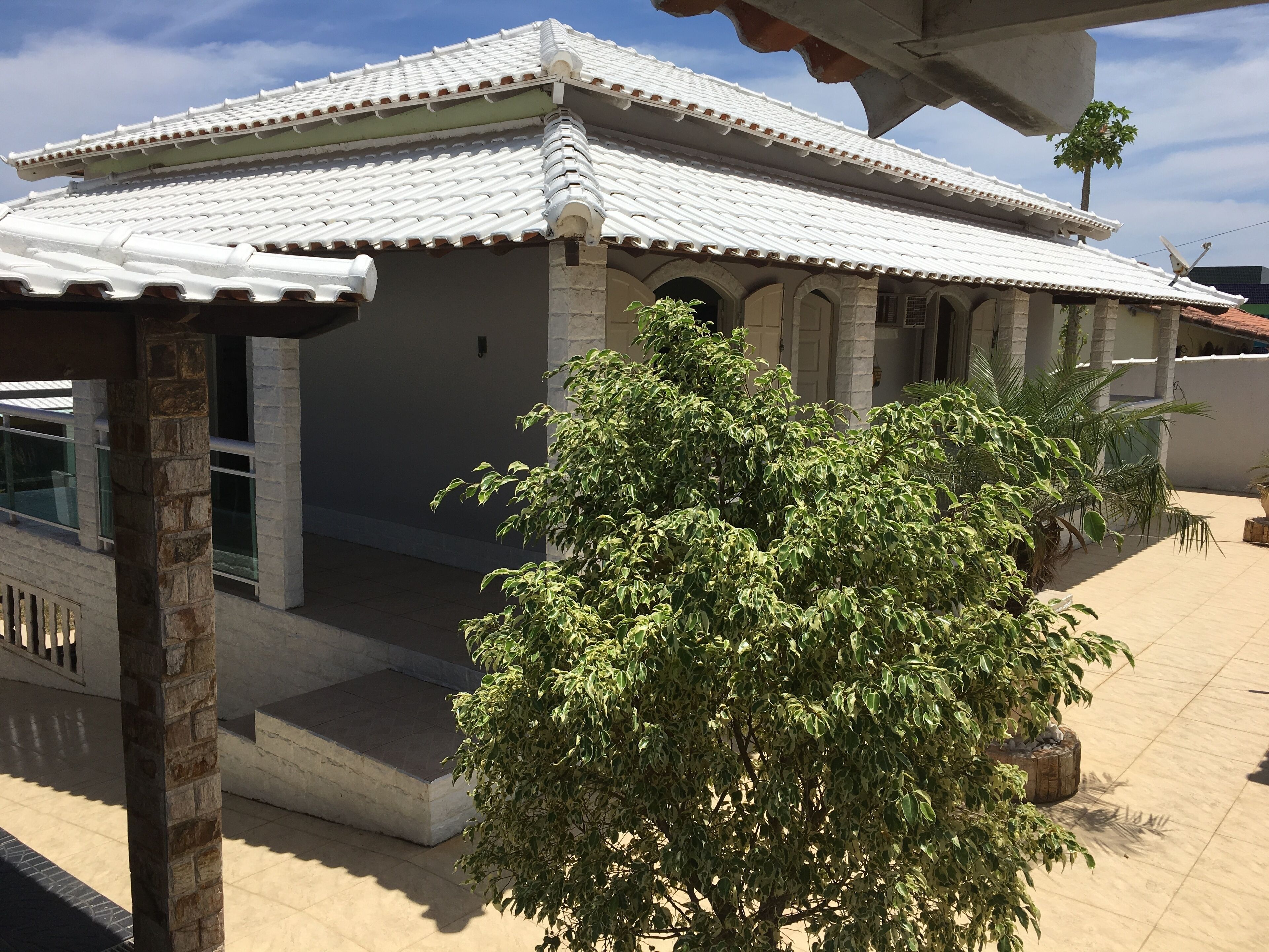 A house with a tiled roof, a covered porch, and a large tree in the foreground.