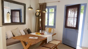 Ein Essbereich mit Holztisch, Bank und Stühlen. Ein Fenster mit Vorhängen, eine Tür mit Glasfenster und ein Spiegel an der Wand sind zu sehen.