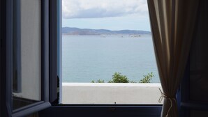 Ein Fenster mit Blick auf ein ruhiges Meer und entferntes Land, Vorhänge halb geschlossen.