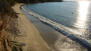 Ein Strand mit sandigem Ufer, klarem Wasser und einigen Gebäuden im Hintergrund.