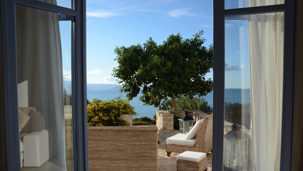 Ein offener Balkon mit Korbmöbeln, Blick auf das Meer und ein Baum.