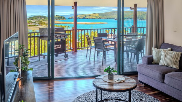 A spacious balcony with a view of a coastal landscape, furnished with a sofa, chairs, and a dining table.