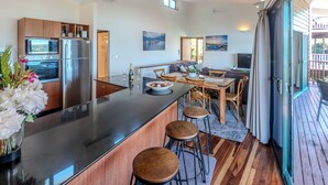A modern kitchen with a central island, wooden bar stools, and a dining area with a table and chairs.