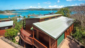 A coastal property with a wooden deck, a covered outdoor area, and a view of the sea and hills.