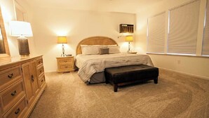 Un dormitorio con cama, mesitas de noche, cómoda, ventilador de techo y ventana con persianas.
