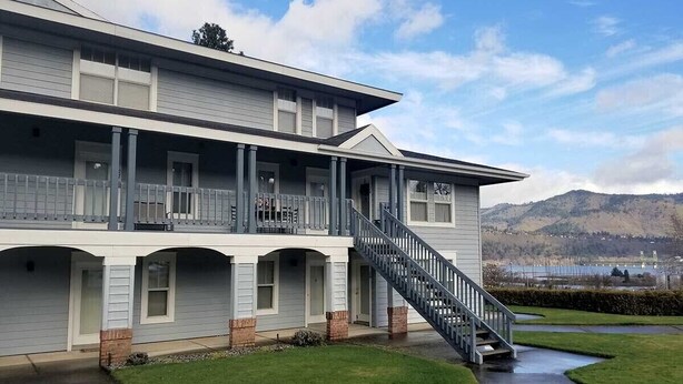 Un edificio de dos pisos con un porche cubierto, una escalera y vistas a un lago y montañas al fondo.