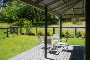 A covered patio with outdoor seating, a view of a grassy area, and a wooden fence.