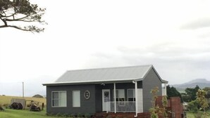 Ein eingeschossiges Haus mit einer Veranda, einem kleinen Garten und einer Bergkulisse im Hintergrund.