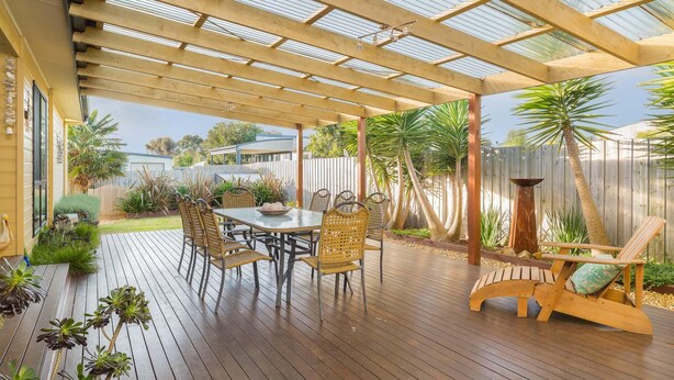 A covered outdoor area with a wooden deck, a table with chairs, and various plants.
