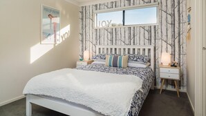 A bedroom with a bed, two bedside tables, a window, and a wall with a 'JOY' sign.