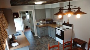 Een keuken met een stenen vloer, houten stoelen, een eettafel en een fornuis.