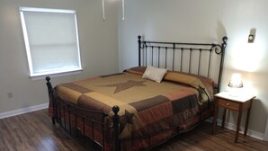 Een slaapkamer met een metalen bedframe, een gewatteerde sprei, een bedlampje en een raam met zonwering.